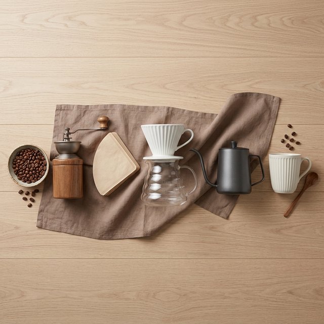 From directly overhead, an unbranded pour-over coffee set with ribbed porcelain and clear borosilicate components arranged in sequence on pale oak; warm taupe background, broad diffused softbox light and gentle side fill shape this commercial product image, no lettering. — Model 15