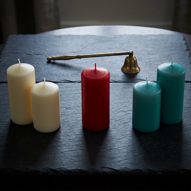 Exactly five candles stand on a dark slate tabletop: two ivory candles on the left, one red candle in the center, and two teal candles on the right. A brass snuffer sits above the red candle, nothing else. — Nano Banana 2.1