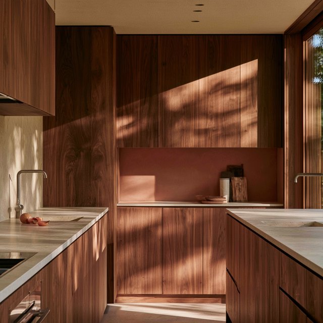 Along a galley kitchen, flat-front walnut cabinets meet pale limestone counters and a matte terracotta backsplash in restrained Scandinavian modern style; soft north-window daylight reveals the worktop from the doorway, with clean aligned lines and believable supports. — Model 13