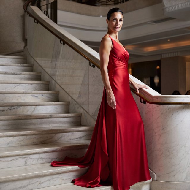 An adult woman in a floor-length red satin evening gown on a marble staircase, soft key light, confident pose, magazine cover style. — ImagineArt 2