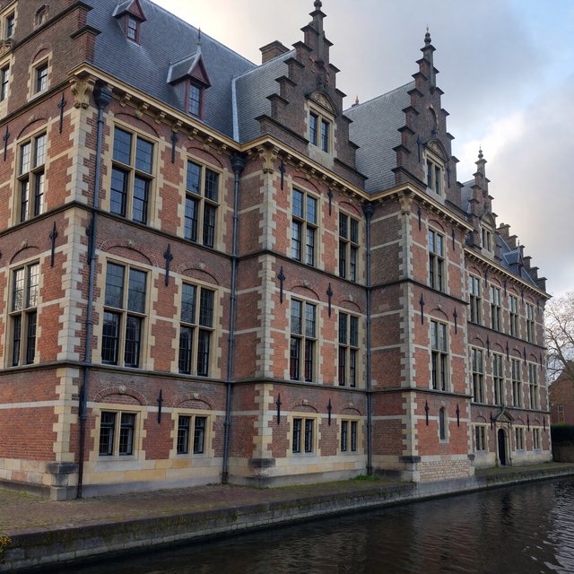 Exterior of a Dutch Renaissance canal-side archive, with warm red brick, pale stone bands, stepped gables, and tall sash windows; soft overcast light reveals the masonry, viewed from the opposite quay, with convincing structure and precise architectural lines. — ImagineArt 1.5 Pro