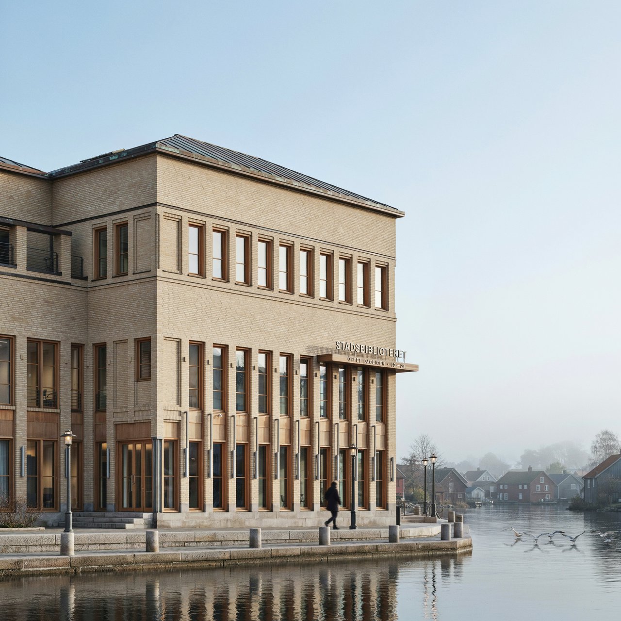 A riverside public library in contemporary Nordic brick architecture combines pale buff brick, oak-framed glazing, and a copper roof; cool morning light grazes its elevations, viewed from across the promenade, with straight lines and credible supports. — Ideogram v4