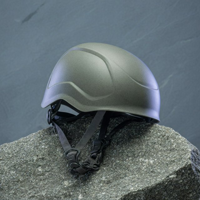 Against a muted slate backdrop, an unbranded climbing helmet with a matte recycled-polymer shell and woven nylon straps rests on rough granite; broad diffused key light and a cool rim light shape this commercial product image, with no lettering. — Grok Imagine Image Quality