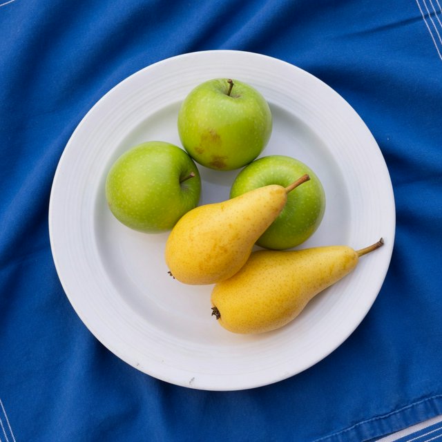 Exactly three green apples and two yellow pears on a white plate, the plate on a blue tablecloth, nothing else on the table. — Grok Imagine Image Quality