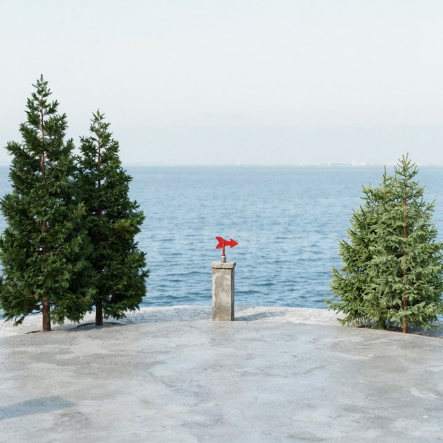 At a coastal overlook, a small red weather vane stands on a stone post. Exactly two dark-green pine trees line the left edge and one pale-green pine tree stands at the right edge; a blue sea fills the background, nothing else. — Model 8