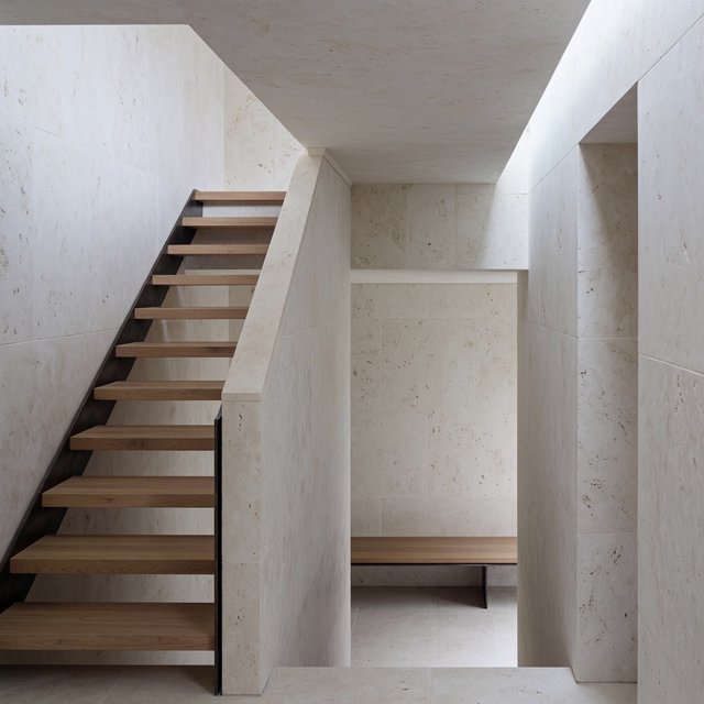 Beneath a pale limestone stairwell, a restrained mid-century modern interior frames a straight oak stair with blackened-steel stringers and limestone landings; afternoon clerestory light, viewed from the upper landing, reveals credible connections and aligned geometry. — Krea 2 Medium