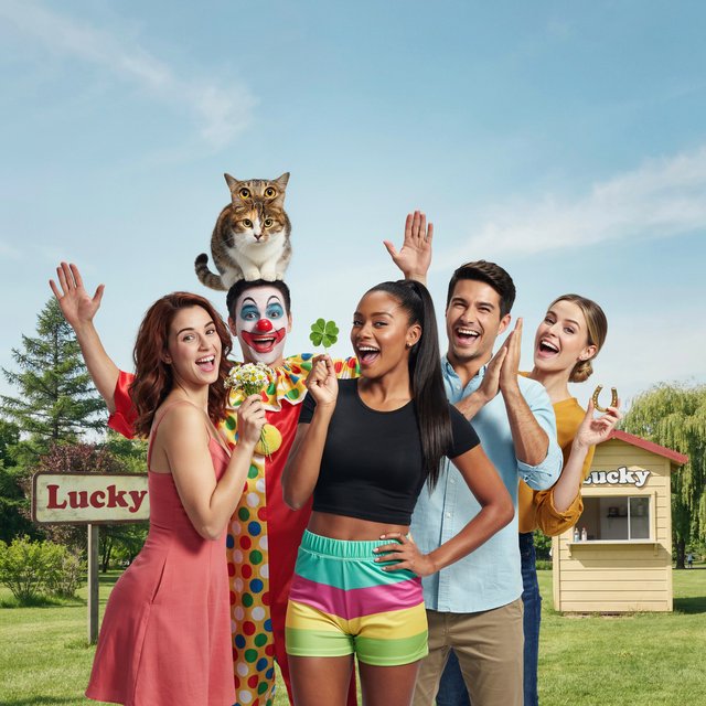 Realistic. Four to five adults having a very lucky day. One of the people is a clown with a very strange cat on their head. Another is wearing a black crop top and multicolored shorts. The word “Lucky” is seen at least twice in the background. — Ideogram v4.5