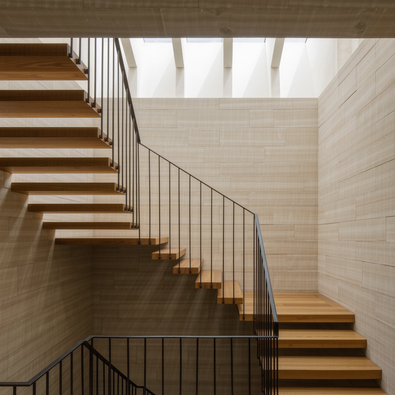 Beneath a pale limestone stairwell, a restrained mid-century modern interior frames a straight oak stair with blackened-steel stringers and limestone landings; afternoon clerestory light, viewed from the upper landing, reveals credible connections and aligned geometry. — Kling v3 Omni