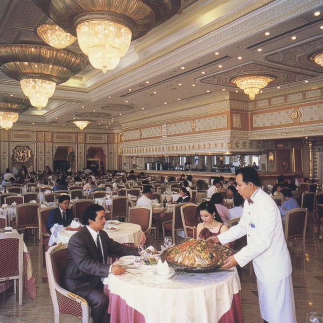 A very posh, well-lit 1990s restaurant with beautiful, tasteful decor. A husband and wife dine in a high-class restaurant. The waiter serves something very surprising as the main course! — Krea 2 Large