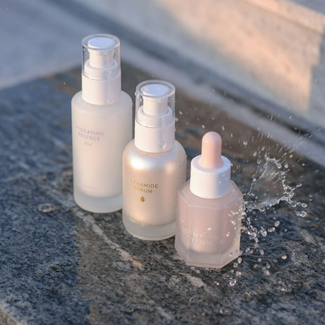 Three frosted glass skincare bottles on a wet stone surface with a splash of water, morning light, shallow depth of field. — Grok Imagine Image Quality