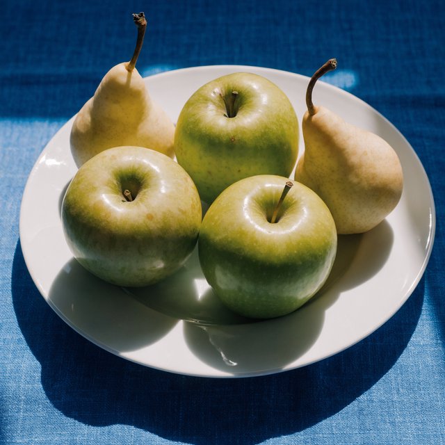 Exactly three green apples and two yellow pears on a white plate, the plate on a blue tablecloth, nothing else on the table. — Recraft v4 Pro
