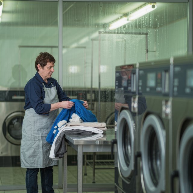 Candid documentary photograph of an adult laundromat attendant sorting warm clothes beside humming machines, cool fluorescent light, 50mm lens with moderate depth of field, loose lint clinging to a blue towel and faint condensation on the glass doors. — Kling v3 Omni