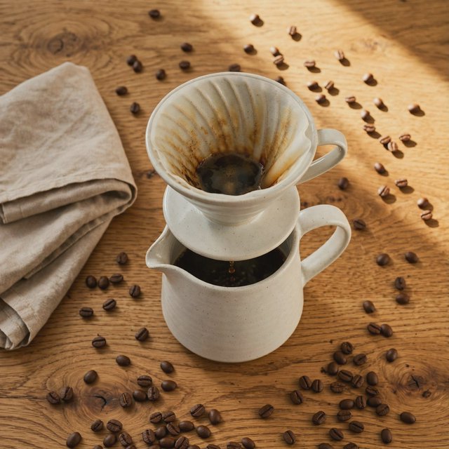 Overhead flat lay of a ceramic pour-over coffee set on oak, roasted beans scattered, a folded linen napkin, warm natural light. — Muse Image 1.0
