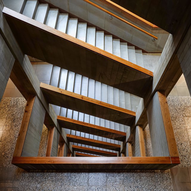 At the heart of a restrained Brutalist museum, a folded concrete stair rises beside smoked-oak handrails and terrazzo landings; skylight washes the treads, seen from the lower landing, with aligned flights and believable supports. — Kling v3