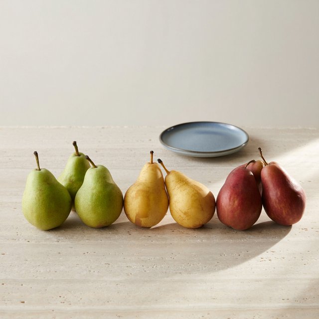 Exactly six ripe pears sit on a pale stone counter: two green pears on the left, two yellow pears in the center, and two red pears on the right. A small blue plate sits above the center pair, nothing else. — ImagineArt 2