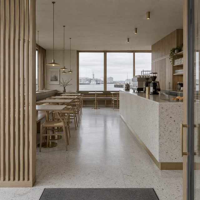 Inside an empty harbor café, restrained Danish modern design pairs ash slat screens, pale terrazzo, and brushed brass; overcast window light reaches the counter, viewed from the entrance, with aligned joinery and believable supports. — Model 3
