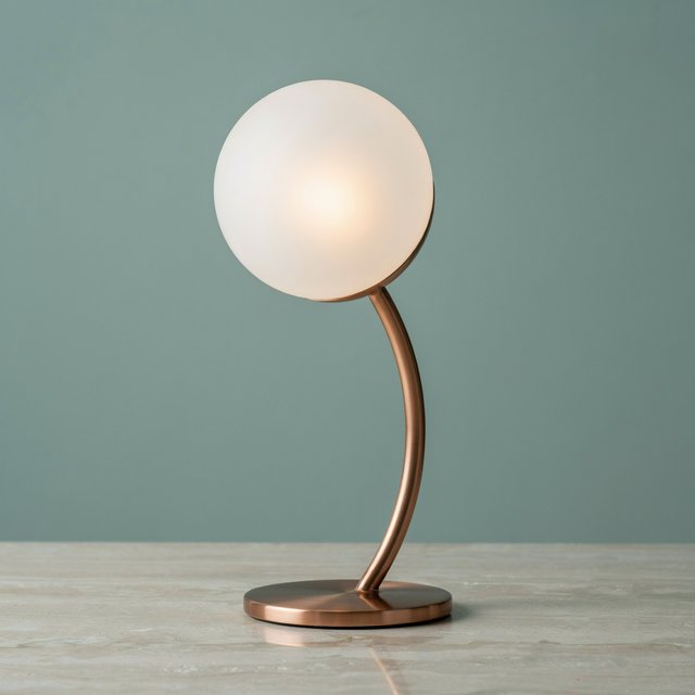 Commercial product photograph of an unbranded sculptural desk lamp with a frosted opal glass globe and brushed copper stem, standing on a pale travertine surface against a muted sage background, illuminated by soft overhead diffusion and a delicate warm rim light. — Ideogram v4