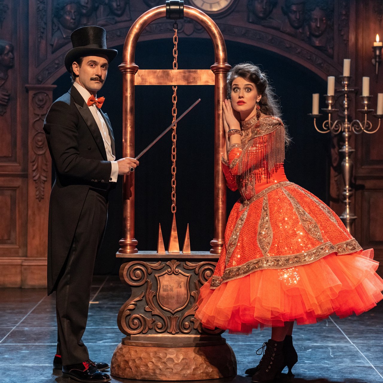 A magician's act on a well-lit stage. A well-dressed magician and glamorous adult female assistant have just unveiled the magician's guillotine. The adult female assistant fakes a worried look, knowing she will shortly participate in the illusion. — Recraft v4 Pro