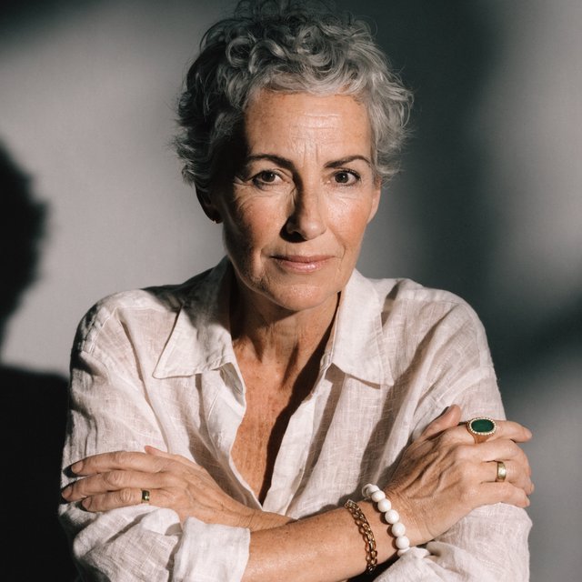 Studio portrait of a woman in her 40s with short grey hair and a linen shirt, Rembrandt lighting, neutral grey backdrop, slight smile. — Recraft v4