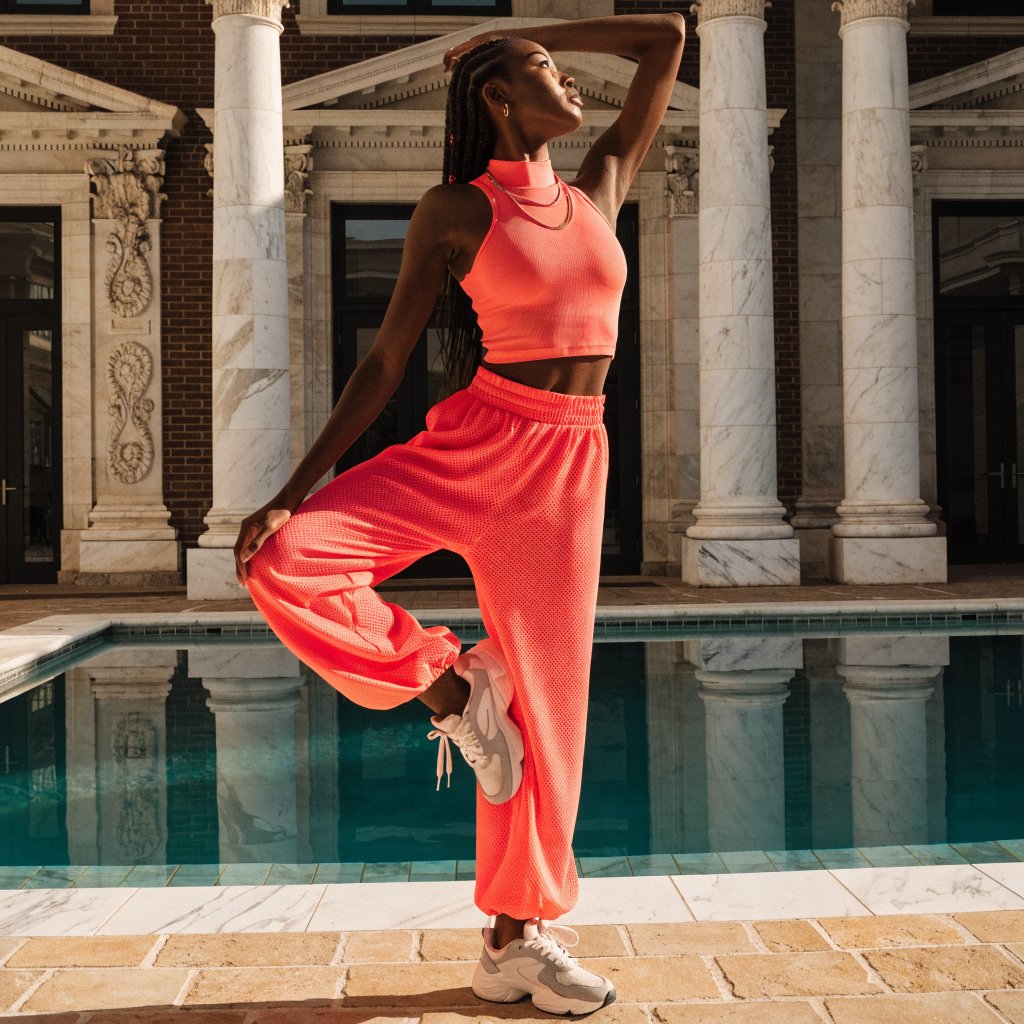 Editorial glamour photograph of one adult woman in coral fitness wear stretching beside a sunlit indoor pool, natural posture, soft reflections, flattering golden light, refined athletic campaign mood. — Recraft v4