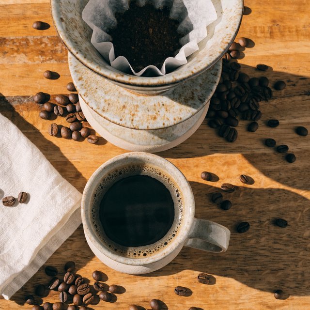 Overhead flat lay of a ceramic pour-over coffee set on oak, roasted beans scattered, a folded linen napkin, warm natural light. — Recraft v4 Pro