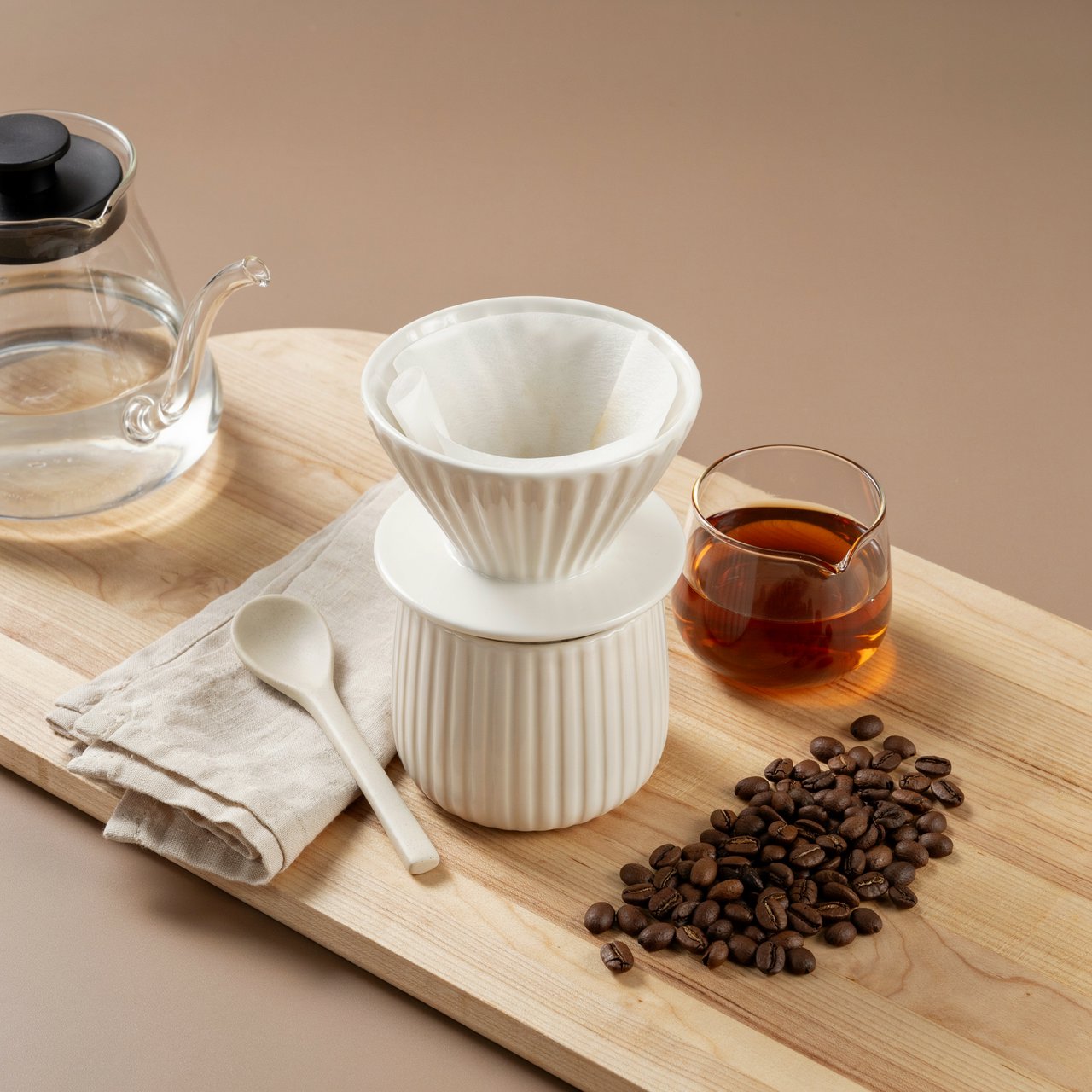 From directly overhead, an unbranded pour-over coffee set with ribbed porcelain and clear borosilicate components arranged in sequence on pale oak; warm taupe background, broad diffused softbox light and gentle side fill shape this commercial product image, no lettering. — Ideogram v4