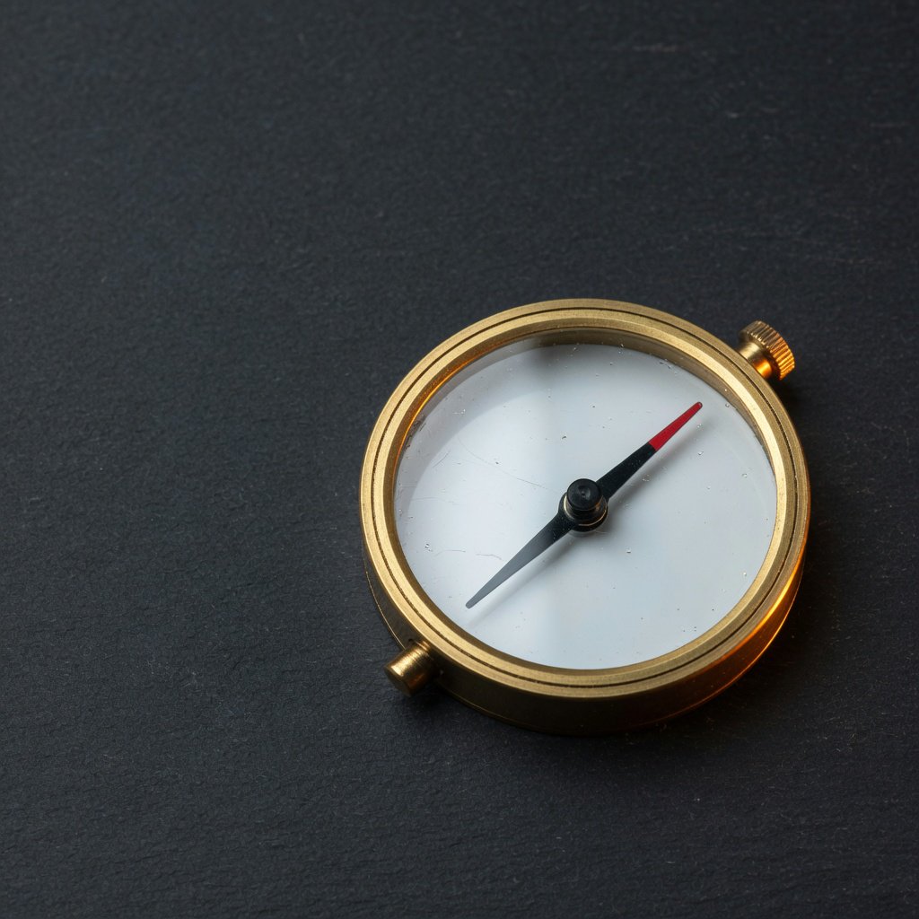 A compact brass pocket compass rests on black slate, its satin-metal casing and clear glass cover catching a broad diffused key and narrow warm rim light against a deep charcoal background; an unbranded commercial product image, blank face without lettering. — Grok Imagine Image Quality