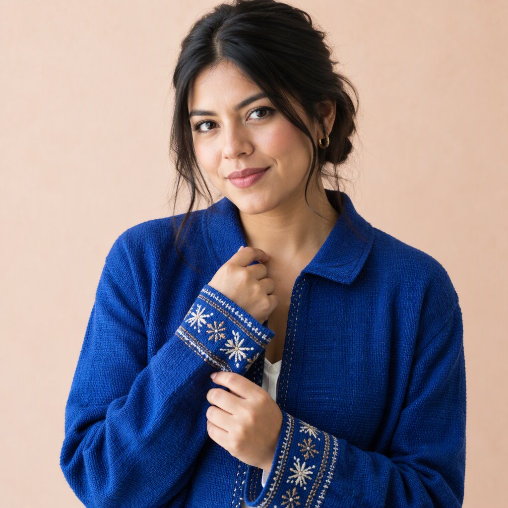 Fashion portrait of an adult Latina woman in her late 20s wearing a handwoven cobalt-blue cotton jacket, one hand touching its embroidered cuff, curious half-smile, against a pale peach studio backdrop, soft diffused window light shaping her face. — GPT Image 2.5 Flare
