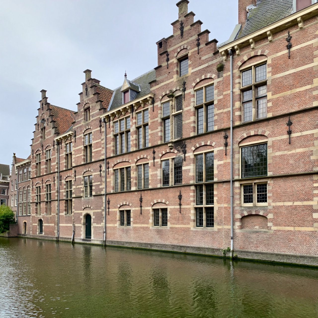 Exterior of a Dutch Renaissance canal-side archive, with warm red brick, pale stone bands, stepped gables, and tall sash windows; soft overcast light reveals the masonry, viewed from the opposite quay, with convincing structure and precise architectural lines. — ImagineArt 2