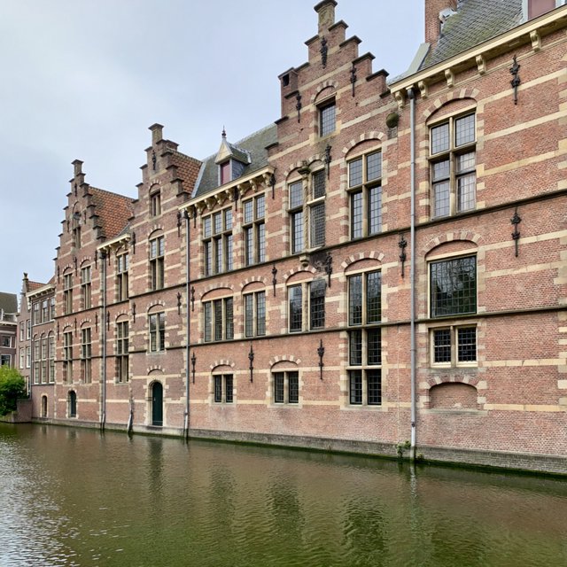 Exterior of a Dutch Renaissance canal-side archive, with warm red brick, pale stone bands, stepped gables, and tall sash windows; soft overcast light reveals the masonry, viewed from the opposite quay, with convincing structure and precise architectural lines. — ImagineArt 2