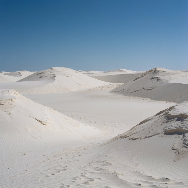A pale gypsum dune field beneath a wind-brushed, cloudless midday sky, fine sand streaming over steep ridges; delicate ripple patterns and scattered salt-tolerant grasses sharpen the foreground as dunes soften toward a distant basin. — Krea 2 Medium