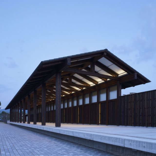 Contemporary Japanese timber train station, charred cedar cladding, pale concrete platform, broad pitched roof with exposed beams and translucent clerestories, cool morning light, viewed obliquely from the quiet approach plaza, precise straight lines and plausible structure. — Kling v3 Omni