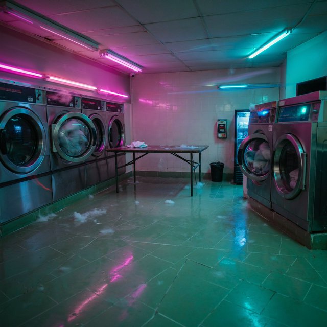 Neon washes a nearly empty overnight laundromat, reflections trembling across tiled floor and spinning steel drums. A handheld street snapshot under magenta and cyan tubes, shot at 35mm with moderate depth of field, catches lint drifting in the air. — Ideogram v4.5