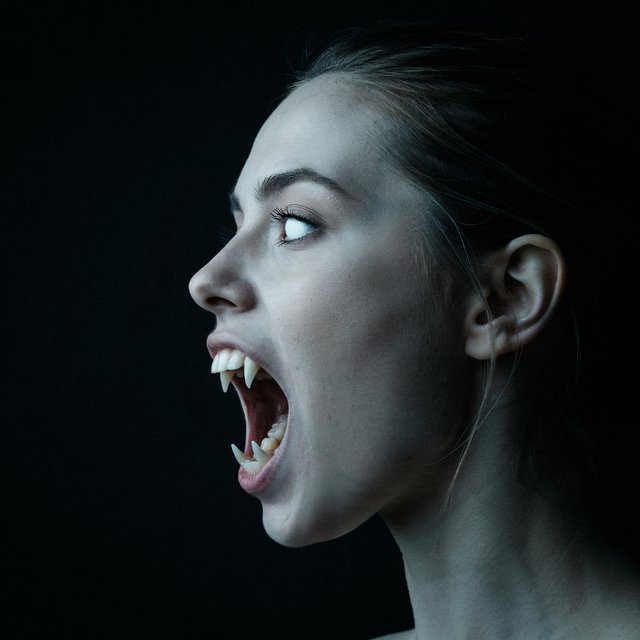 A creepy woman in side profile. Focus on the head with a slightly alien figure. Pale skin. No irises in the eyes. Mouth is open wide with very sharp, long razor teeth. Black background. Chiaroscuro effect. — Ideogram v4
