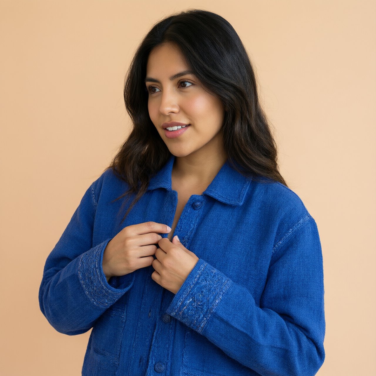 Fashion portrait of an adult Latina woman in her late 20s wearing a handwoven cobalt-blue cotton jacket, one hand touching its embroidered cuff, curious half-smile, against a pale peach studio backdrop, soft diffused window light shaping her face. — Qwen Image 3.0