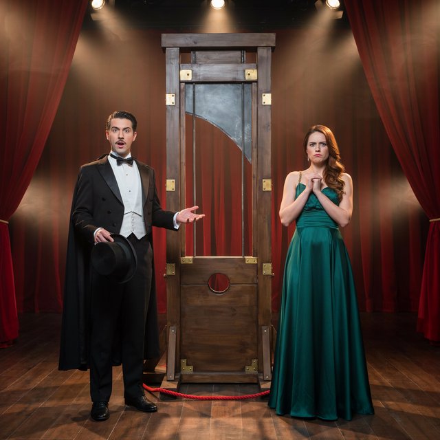 A magician's act on a well-lit stage. A well-dressed magician and glamorous adult female assistant have just unveiled the magician's guillotine. The adult female assistant fakes a worried look, knowing she will shortly participate in the illusion. — Ideogram v4.5