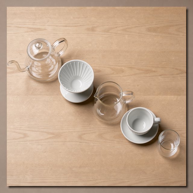 From directly overhead, an unbranded pour-over coffee set with ribbed porcelain and clear borosilicate components arranged in sequence on pale oak; warm taupe background, broad diffused softbox light and gentle side fill shape this commercial product image, no lettering. — Model 1