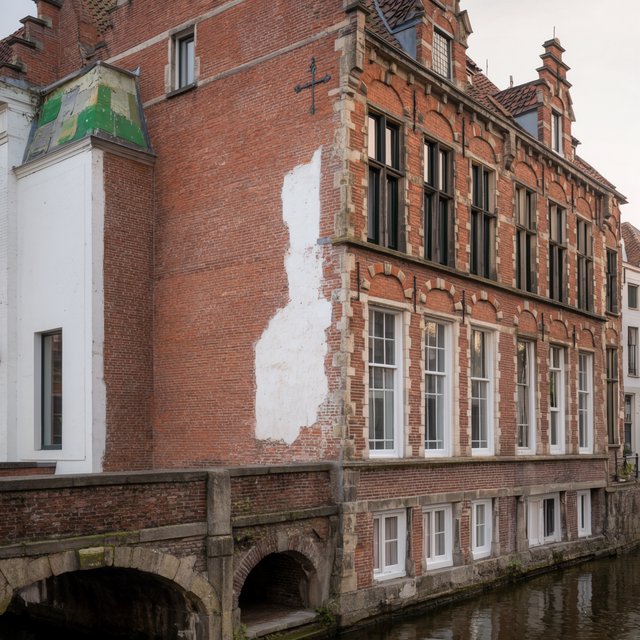 Exterior of a Dutch Renaissance canal-side archive, with warm red brick, pale stone bands, stepped gables, and tall sash windows; soft overcast light reveals the masonry, viewed from the opposite quay, with convincing structure and precise architectural lines. — Krea 2 Large
