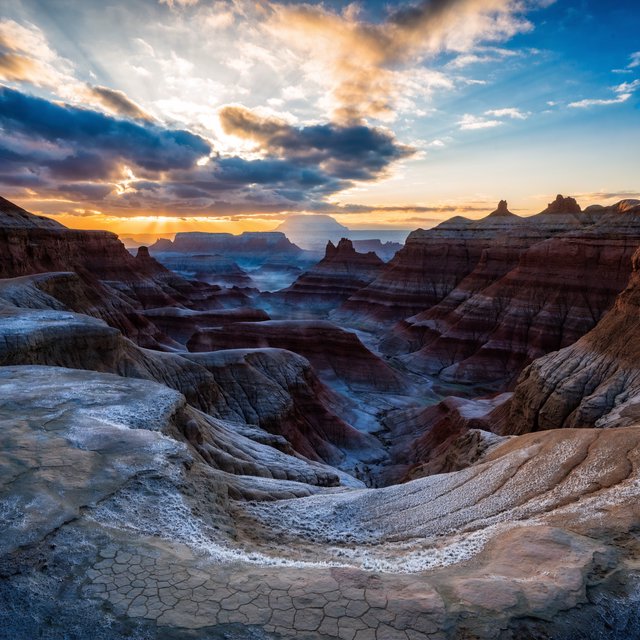 A red-sandstone badlands plateau beneath clearing winter clouds at sunrise, overnight frost silvering the gullies; cracked clay and wind-smoothed rock lead the eye across layered mesas fading into pale distance. — Recraft v4 Pro