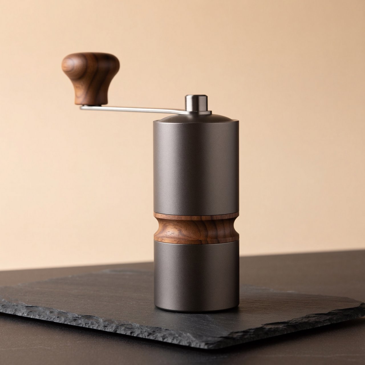 Commercial product photograph of an unbranded portable espresso grinder crafted from anodized aluminum with walnut accents, resting on a black stone surface against a warm beige background, illuminated by broad diffused studio light and a subtle edge highlight. — ImagineArt 2
