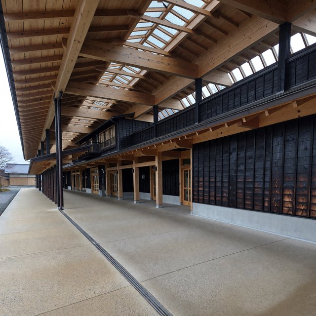 Contemporary Japanese timber train station, charred cedar cladding, pale concrete platform, broad pitched roof with exposed beams and translucent clerestories, cool morning light, viewed obliquely from the quiet approach plaza, precise straight lines and plausible structure. — ImagineArt 1.5 Pro