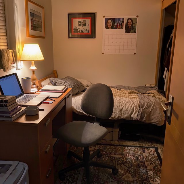 A dorm room belonging to an adult woman, photographed with a cell phone. The camera is sitting on a desk facing the empty chair and the rest of the room. — Kling v3
