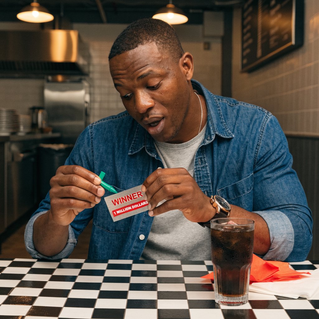 A realistic scene of a random adult person, either Black, white, or Asian, scratching a scratch ticket and discovering that they have won one million dollars. — Recraft v4