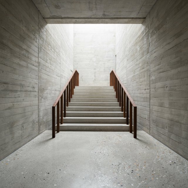 At the heart of a restrained Brutalist museum, a folded concrete stair rises beside smoked-oak handrails and terrazzo landings; skylight washes the treads, seen from the lower landing, with aligned flights and believable supports. — Ideogram v4.5