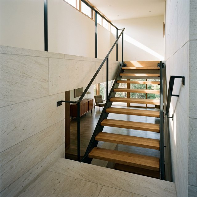 Beneath a pale limestone stairwell, a restrained mid-century modern interior frames a straight oak stair with blackened-steel stringers and limestone landings; afternoon clerestory light, viewed from the upper landing, reveals credible connections and aligned geometry. — Nano Banana 2.1