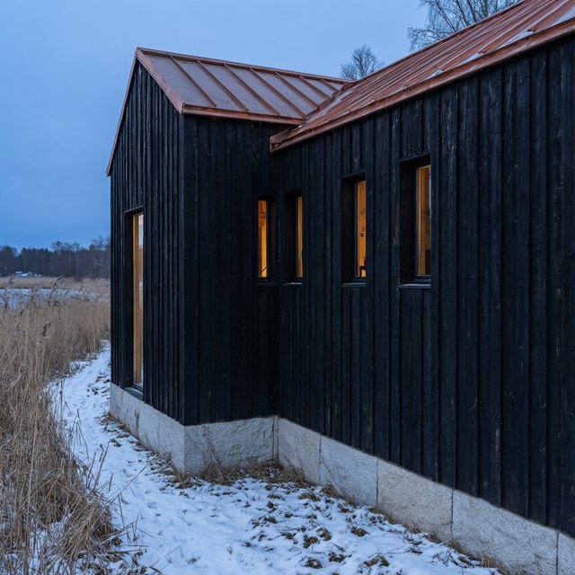 Exterior of a Scandinavian modernist lakeside sauna pavilion, blackened timber cladding, pale granite plinth, copper roof, winter blue-hour light glowing through narrow windows, viewed from a snowy reed-lined path, straight structural geometry and plausible construction. — Qwen Image 3.0 Pro