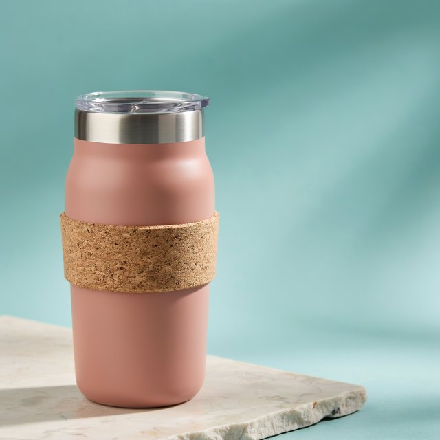 Commercial product photograph of an unbranded insulated travel mug made from matte terracotta powder-coated steel with a cork grip, standing on a pale limestone slab against a soft teal background, lit by broad diffused window light and a gentle edge light. — Ideogram v4