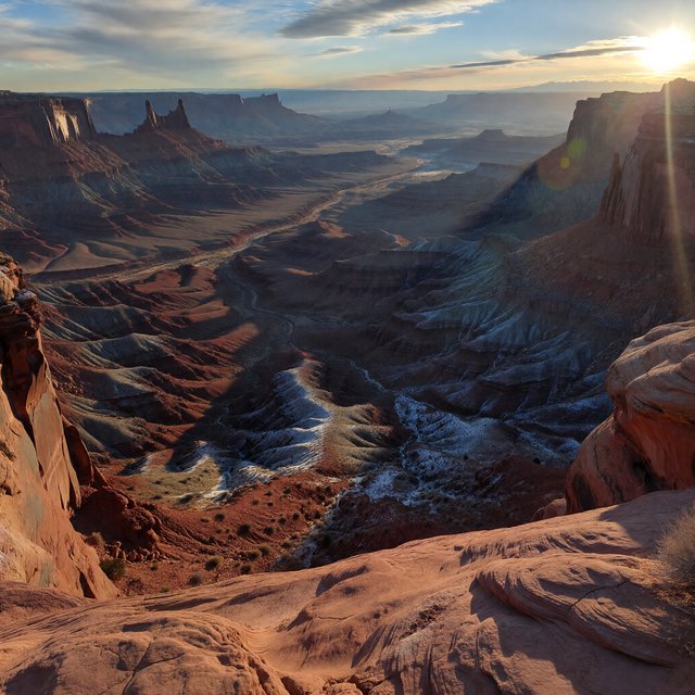 A red-sandstone badlands plateau beneath clearing winter clouds at sunrise, overnight frost silvering the gullies; cracked clay and wind-smoothed rock lead the eye across layered mesas fading into pale distance. — ImagineArt 1.5 Pro
