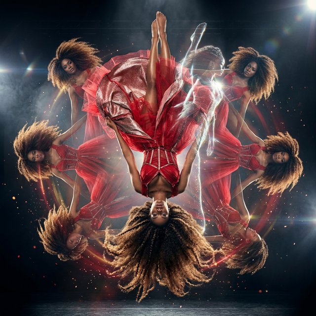 Image of a pop-dance African-American diva. The woman hangs completely inverted in mid-air, head pointing toward the floor and legs toward the ceiling. Her huge hair falls and spreads dramatically in the opposite direction, while her expression remains cool and composed. Her red gown is turned inside out, exposing its sparkling lining, seams, and construction. To push the surrealism further, a second, reversed version of her silhouette appears to peel outward from her original form, like a three-dimensional reflection escaping its owner. Multiple copies of the woman circle around a central point, each rotated to a different angle. Their flowing hair and red gowns form a pinwheel or circular vortex, creating the impression that one woman is spinning endlessly around herself. — Nano Banana 2.1