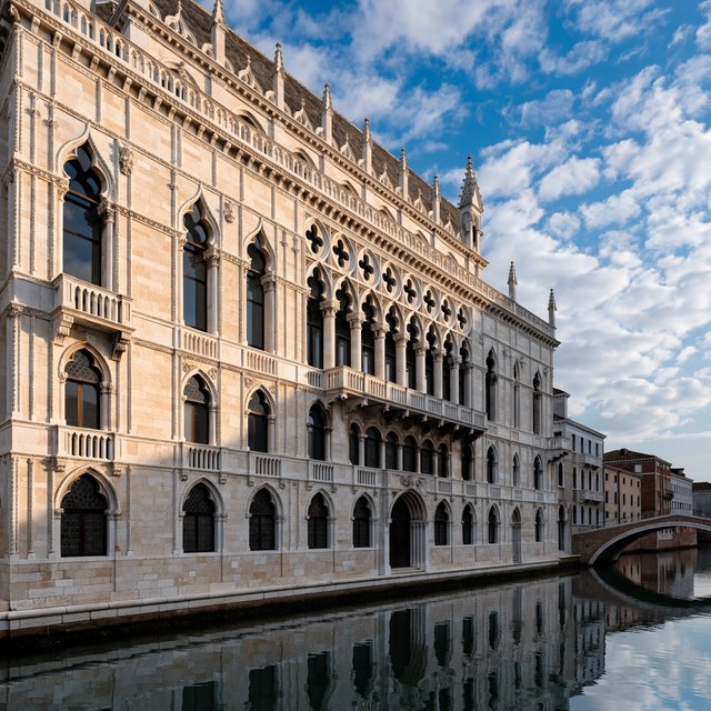 Exterior of a Venetian Gothic opera house beside a quiet canal, pale Istrian limestone, pointed arches, quatrefoil tracery, and a steep slate roof; cool morning light, viewed from across the water, crisp masonry lines and believable structure. — Recraft v4 Pro